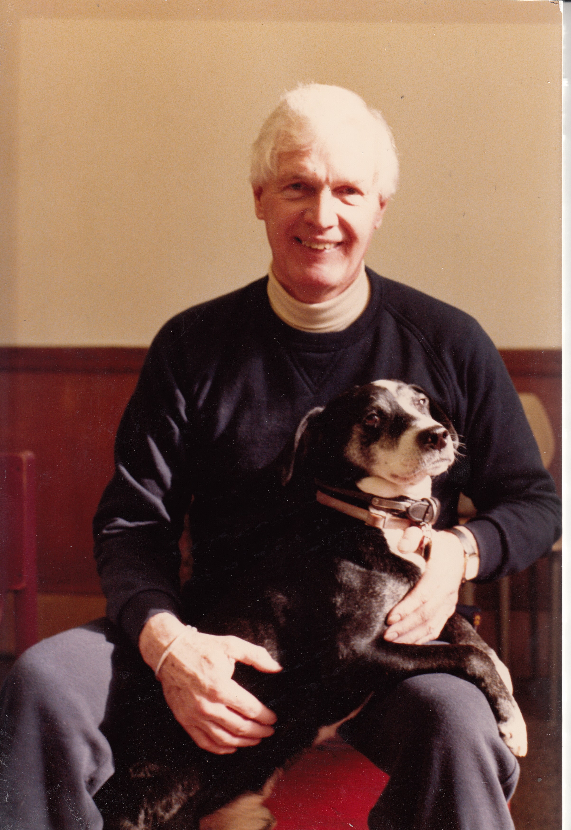 Jack McAllister smiles in the evening light, with his dog Hero on his lap.